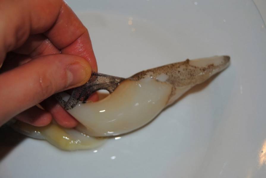 2. У свежих кальмаров кожица сходит так, как показано на картинке. Очищенные кальмары промойте, разрежьте на две части и затем еще резаните поперек. На кожице острым ножом можете сделать надрезы, чтобы у готовых кальмаров получился красивый узор на внешней части. На сковороду капните немного масла, хорошенько его разогрейте и обжарьте кальмары в течение 1-2 минут. Затем выложите на блюдо.