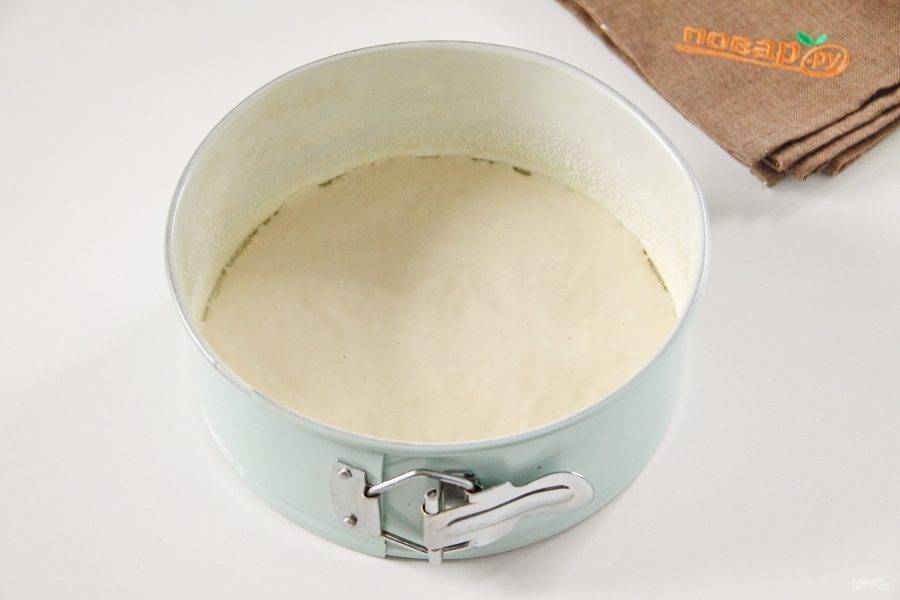 7. Форму для выпечки смажьте маслом и присыпьте манкой или мукой. Вылейте половину порции теста и разровняйте его ложкой.
