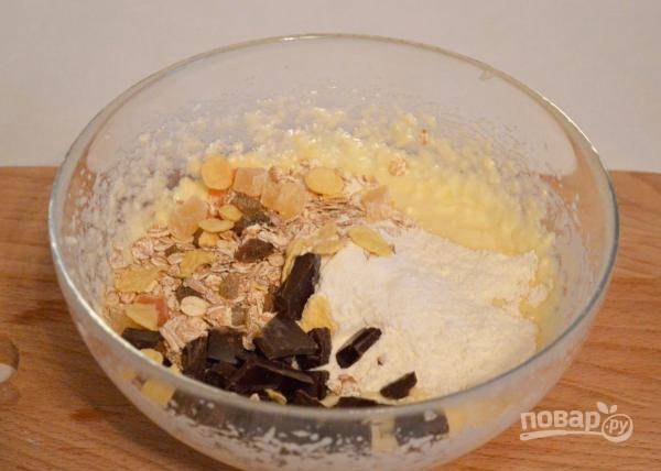 Затем добавьте половину мюсли, муку с разрыхлителем и поломанный на кусочки шоколад. Перемешайте тесто.