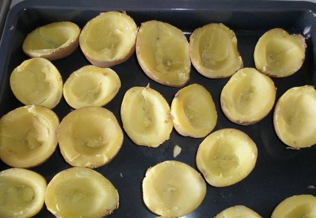 Картофель промойте и отварите в мундирах до готовности. Затем остудите и разрежьте на половинки. Аккуратно, при  помощи ложки, извлекаем мякоть, делая в картошке углубления. Мякоть нам еще пригодится.