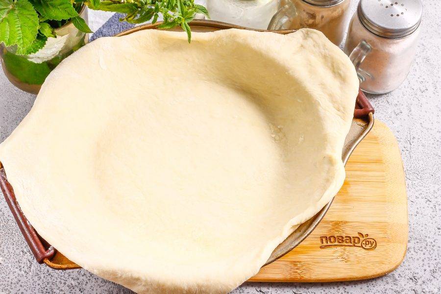 Раскатайте тесто в округлый пласт. Форму для выпекания смажьте маслом. Выложите в нее тесто, заходя за края.