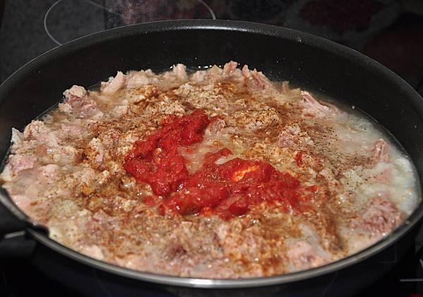 4. Тушенку отправляем на сковороду, добавляем к ней выдавленный чеснок и томатную пасту. Жарим, постоянно помешивая, и когда испарится лишняя жидкость, отправляем начинку в жаровню, где варится каша.