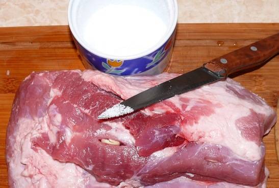 Нож опускаем в соль и делаем в мясе много надрезов, в которые вставляем чеснок.