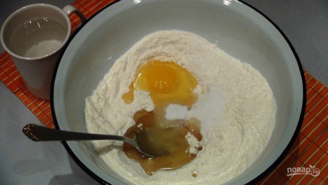 Приготовим тесто для основы. Смешаиваем масло, воду и яйцо. Туда же добавляем дрожжи, перемешиваем. По вкусу добавьте соль. Начинайте вводить муку и замешивать тесто.