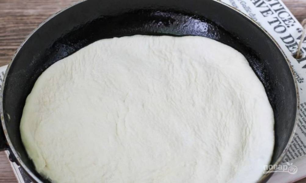 Смажьте сковородку растительным маслом и разогрейте на плите. Затем раскатайте тесто в тоненький пласт и вырежьте из него круг по размеру сковороды. Остатки теста можно положить в морозилку. Выложите корж на сковороду. 