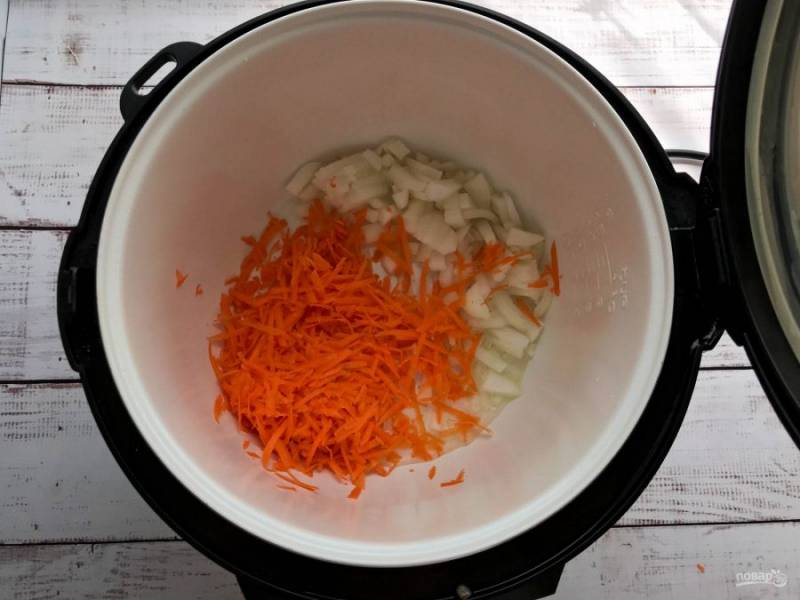 В чашу мультиварки налейте растительное масло, выложите тертую морковь, нарезанный лук и включите режим "Жарка" на 5-7 минут. 