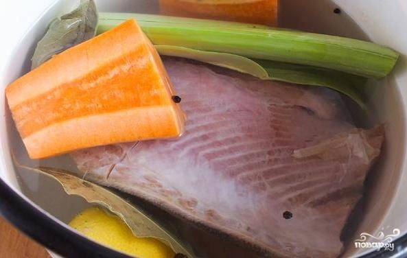 Морковь очистите, помойте и нарежьте большими кусками вместе с лимоном и луком. Эти ингредиенты, а также рыбу, лавровый лист и перцы залейте двумя литрами воды в кастрюле.