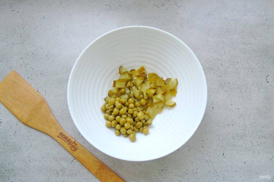 Консервированный зеленый горошек выложите в салатник. Добавьте нарезанный соленый или маринованный огурец.