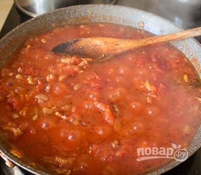 Затем добавьте измельчённый чеснок и травы. Жарьте ещё пару минут. Затем добавьте томаты в собственном соку, сахар, соль и перец. Доведите соус до кипения.