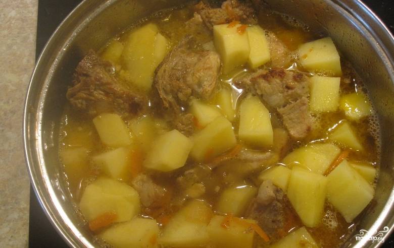 Картофель очищаем, нарезаем кубиками и складываем в кастрюлю к мясу. Доливаем воду так, чтобы покрыть картофель. Доведите блюдо до кипения, убавьте огонь, продолжайте тушить под крышкой еще 10-15 минут.