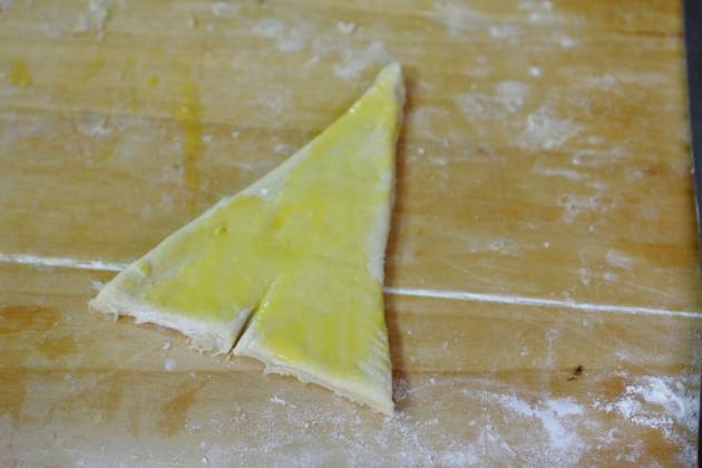 Снова помещаем тесто в холодильник на 30 минут. Нарезаем на треугольники, сворачиваем в рулетики, начиная с широкого края. Смазываем желтком.