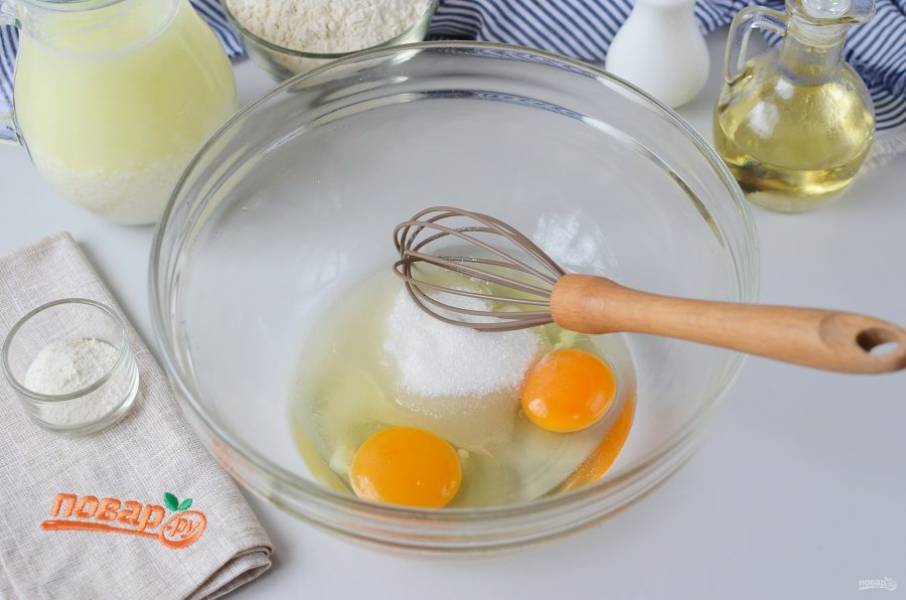 В большую миску разбейте два крупных яйца, добавьте сахар, соль, растительное масло. Венчиком хорошо взбейте массу.