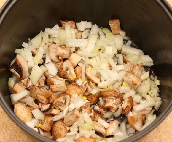 В чашу мультиварки наливаем немного растительного масла и выкладываем в нее нарезанные лук и грибы. Включаем режим "Выпечка" и обжариваем все в течение 10 минут. Перекладываем грибы и лук в тарелку.