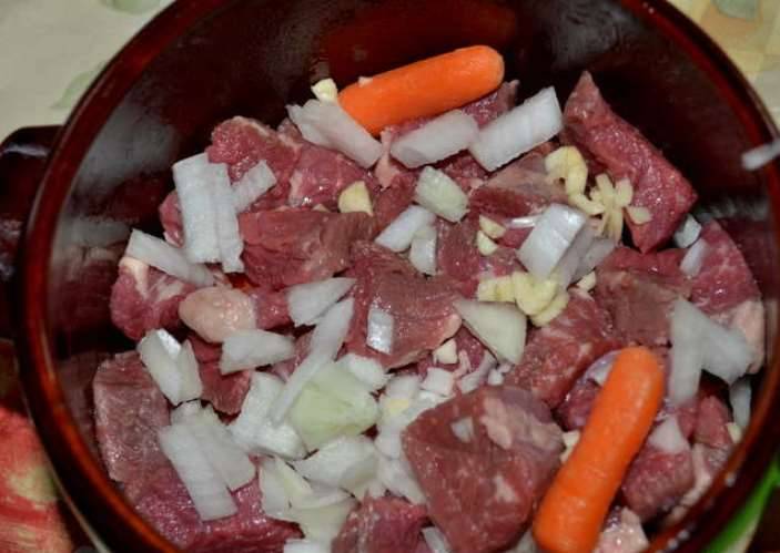 Порежьте на небольшие куски говядину, морковь, лук и чеснок. Сложите их вместе в горшочек. 