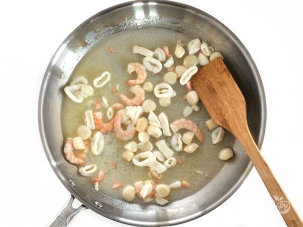 1. На сковороде с высокими бортами растопите половину сливочного масла. Выложите очищенный чеснок и обжарьте его минуту. Выложите микс морепродуктов и жарьте, помешивая, 3-5 минут. 