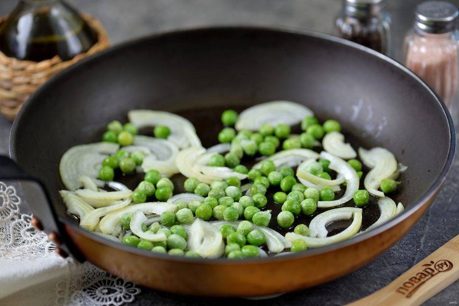 Разогрейте в сковороде растительное масло, выложите в него нарезанный полукольцами репчатый лук, добавьте зеленый горошек. Обжарьте овощи на умеренном огне минуты 3. 