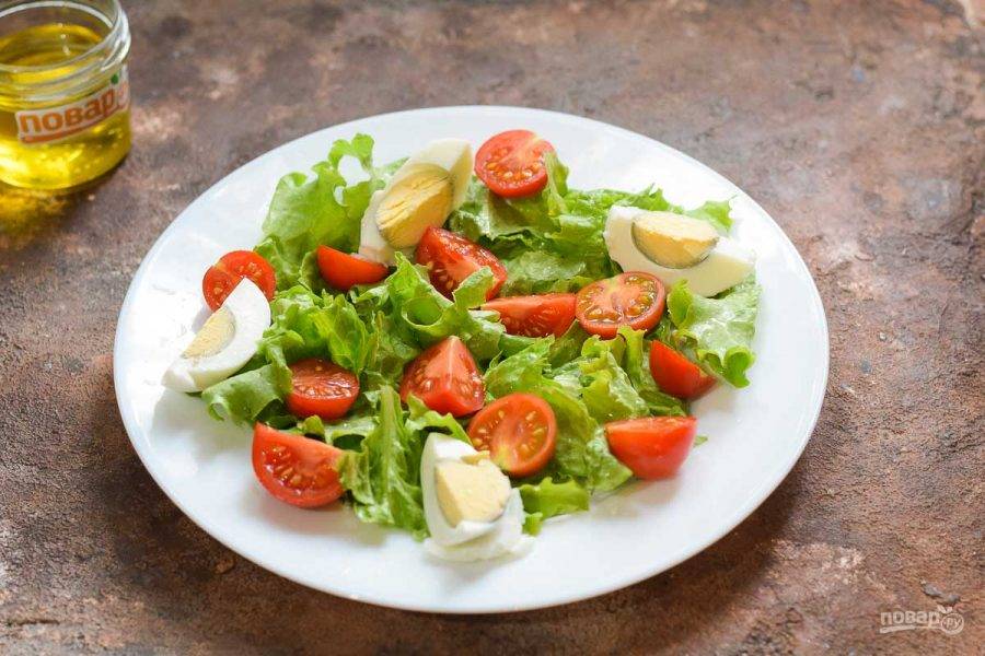 Салатные листья ополосните и просушите, порвите руками и выложите на тарелку. Помидоры разрежьте пополам и выложите на салатные листья. Вареное яйцо очистите и нарежьте на 4 части, добавьте в салат.