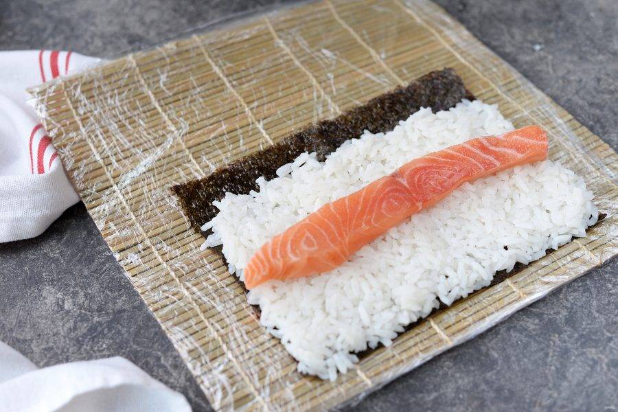На лист нори выложите заправленный рис, посередине на него выложите ломтик свежего лосося.
