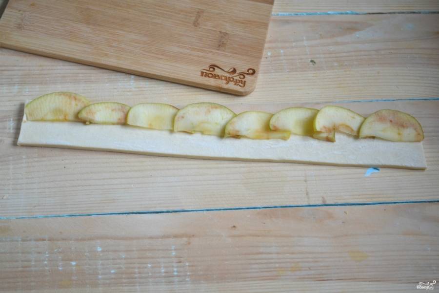 Тесто разморозьте и раскатайте до толщины 2-3 мм. Порежьте его на полоски шириной около 3 см. Выложите яблочные дольки внахлест, как показано на фото.