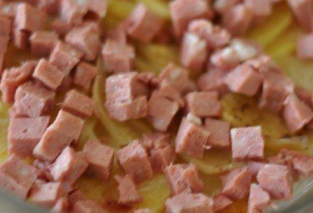 Когда картошка станет мягкой, вынимаем форму из духовки. Колбаску режем на небольшие кусочки и выкладываем ее поверх картофеля. 