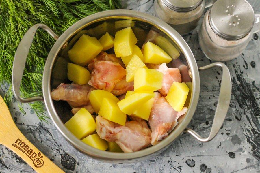 Промойте части курицы и выложите их в кастрюлю. Очистите картофель от кожуры, промойте в воде и нарежьте средними кубиками в емкость. Влейте горячую воду, всыпьте соль и лавровые листья. Поместите кастрюлю на плиту и доведите ее содержимое до кипения, снимите образовавшуюся пену вместе с жиром. Отварите в течение 15 минут.