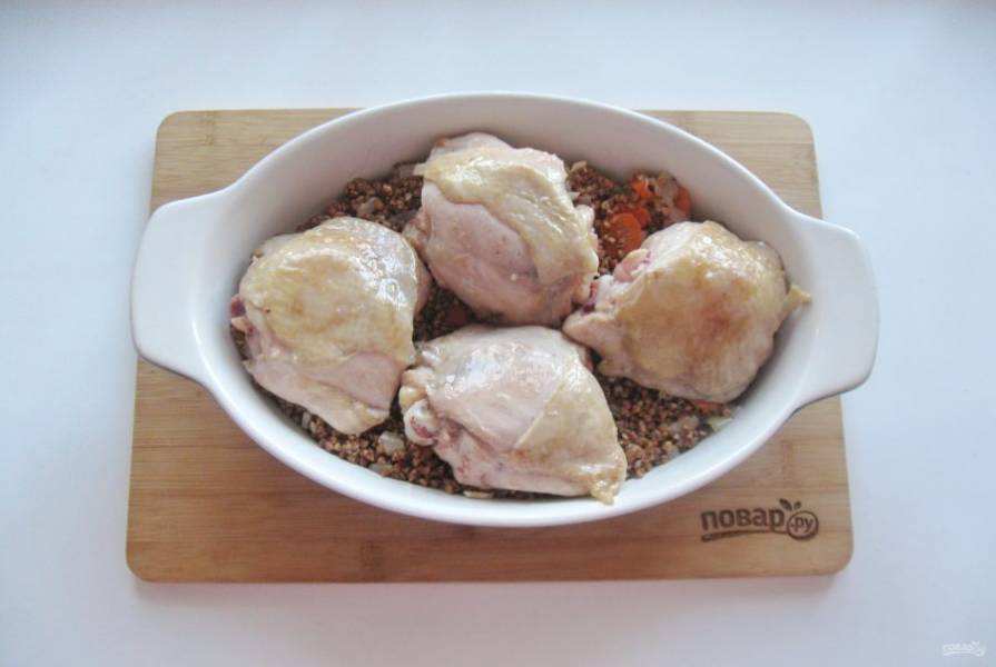 На гречку с овощами выложите куриные бедра, посолите и поперчите мясо.