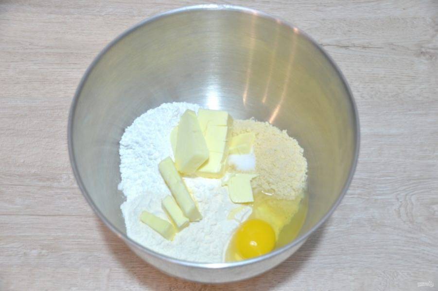 В емкость для взбивания всыпьте муку (пшеничную и миндальную), добавьте соль, 70 грамм сахарной пудры, нарезанное кубиком холодное сливочное масло, вбейте 1 яйцо. 