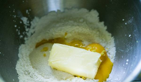 2. Аккуратно отделите желтки и добавьте их в тесто (белки отложите, они нам понадобятся). Всыпьте сахар, выложите сливочное масло. Также для аромата в рецепт приготовления песочного пирога с черной смородиной можно добавить немного цедры апельсина или лимона. Перемешайте все как следует до однородности.