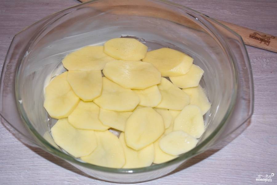 Форму для запекания нужно смазать маслом. Выложите тонко нарезанный сырой картофель кружочками в один слой. Картофель действительно нужно нарезать тонко, иначе при запекании он не приготовится и останется сырым.