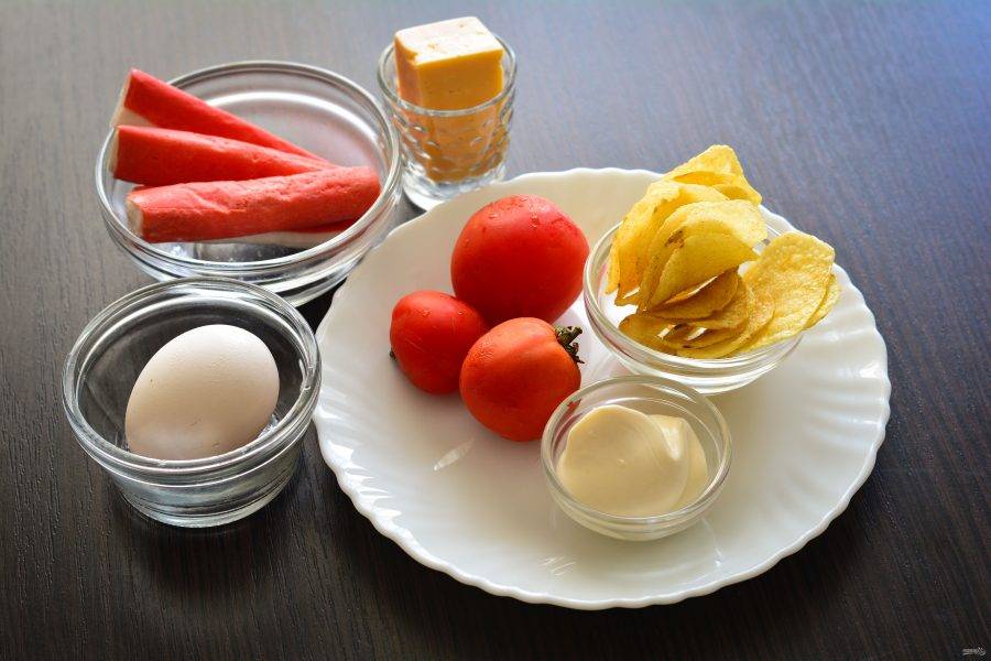 Подготовьте ингредиенты для приготовления салата с чипсами, крабовыми палочками и помидорами.