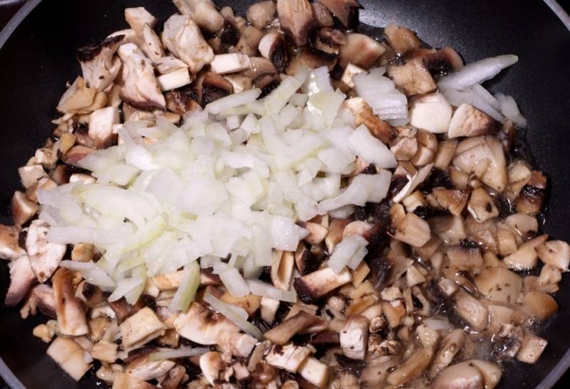 Выкладываем грибы на сковороду и жарим их пару минут, затем добавляем нарезанный лук и жарим все, пока из шампиньонов не выпарится лишняя влага. Начинка готова, ее остается немного посолить и поперчить.