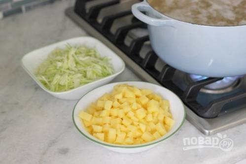 Потом добавьте в бульон картофель, порезанный кубиками, и нашинкованную капусту. Также внесите перец горошком, лавровый лист и соль.