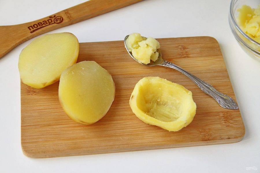 Картофель очистите и разрежьте пополам. При помощи ложечки аккуратно извлеките мякоть, чтобы получились своеобразные "лодочки".