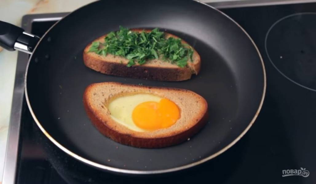 3. Затем переверните и в тот ломтик, где вырезан круг, добавьте яйцо и посолите. На другой ломтик положите мелко нарезанную зелень и тертый сыр. Накройте сковороду крышкой и оставьте на несколько минут.  