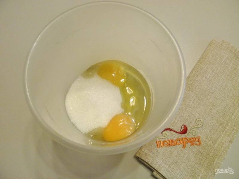 2. Возьмите удобную тару для смешивания продуктов миксером. Вбейте два яйца и сахар, миксером смешивайте до увеличения массы в три раза. Также поменяется цвет на белый.