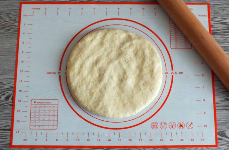 По истечении времени тесто незначительно увеличится в объеме. Не обминая переложите его на рабочую поверхность. Раскатайте в тонкий пласт диаметром 30 см.