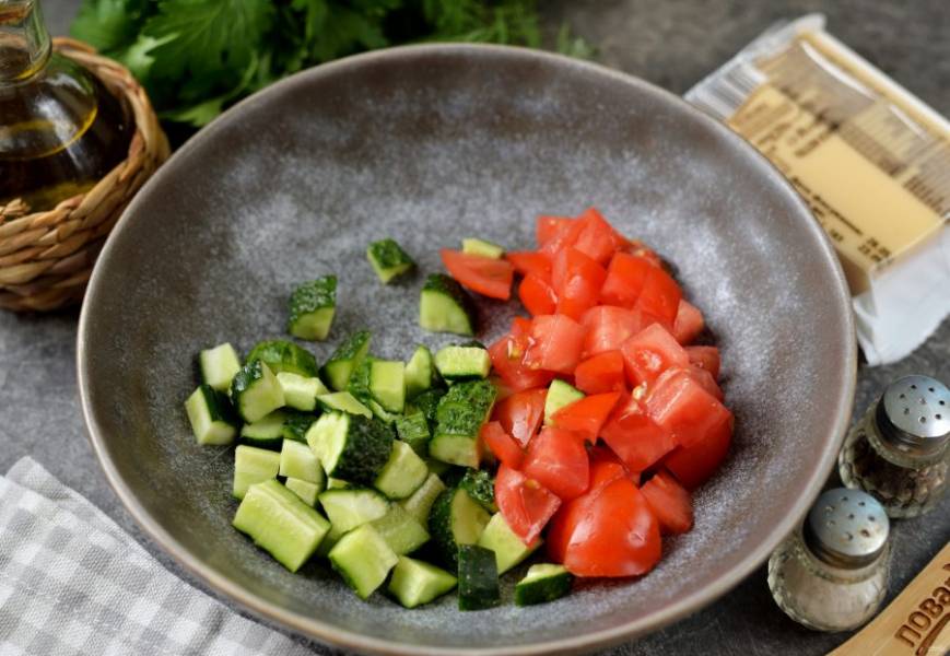 Срежьте кончики на огурцах, вырежьте место плодоножки на помидорах, нарежьте овощи кубиком, переложите в глубокую миску. 