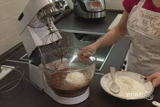 4. В шоколадную массу добавьте кефир и пару ложек муки. Взбивайте 2-3 минуты. После этого отправьте в тесто половину муки и соду, гашенную уксусом. Перемешайте, высыпьте остаток муки и завершите перемешивать тесто. 