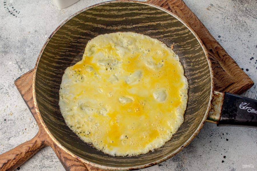 По одному пожарьте яичные блины, для этого яйцо взбиваем вилкой до однородности. Солим смесь. Вливаем в сковороду с небольшим количеством масла и жарим с одной стороны 1,5 минуты и 30 секунд со второй. Переложите блины на блюдо.