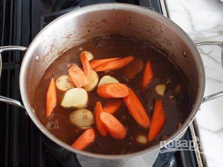 5. Вымойте и очистите морковь, нарежьте её крупными кусочками. Молодой картофель можно не чистить. Выложите овощи к мясу. Продолжайте тушить до готовности. 
Перед подачей можно добавить свежей зелени. 