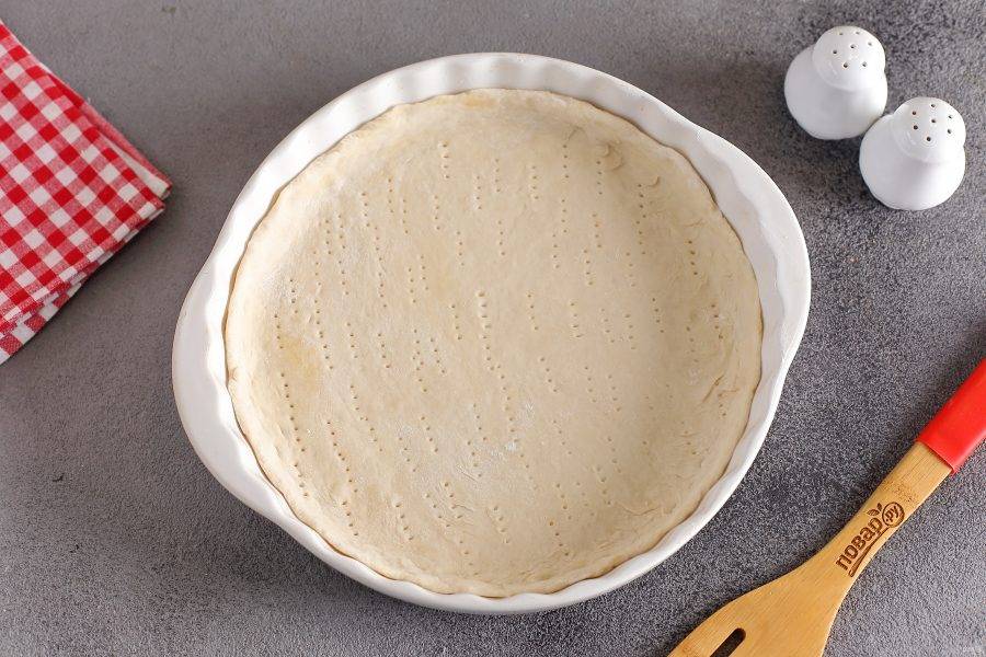Подошедшее тесто разделите на 4 или 6 частей, в зависимости от желаемого размера пиццы. Каждый кусок раскатайте в форме круга, толщиной 2-3 мм. и переложите в смазанную маслом форму или на противень. Тесто наколите вилкой.