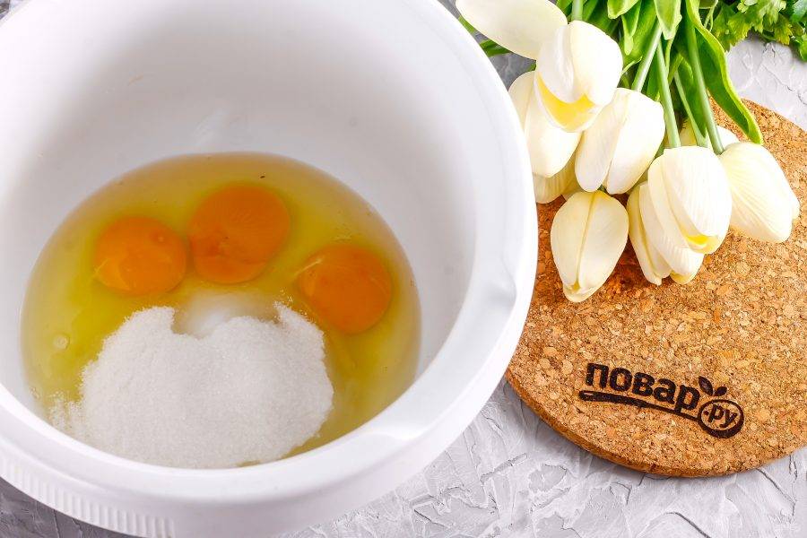 Вбейте куриные яйца в чашу кухонного комбайна или в глубокую емкость. Всыпьте туда же сахар и соль. Взбейте все примерно 3-4 минуты на самой высокой скорости техники.