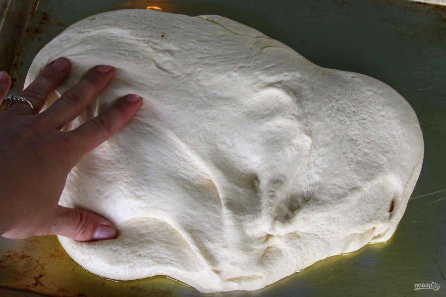 8.	Выложите тесто на противень с оливковым маслом и руками разровняйте его по форме.