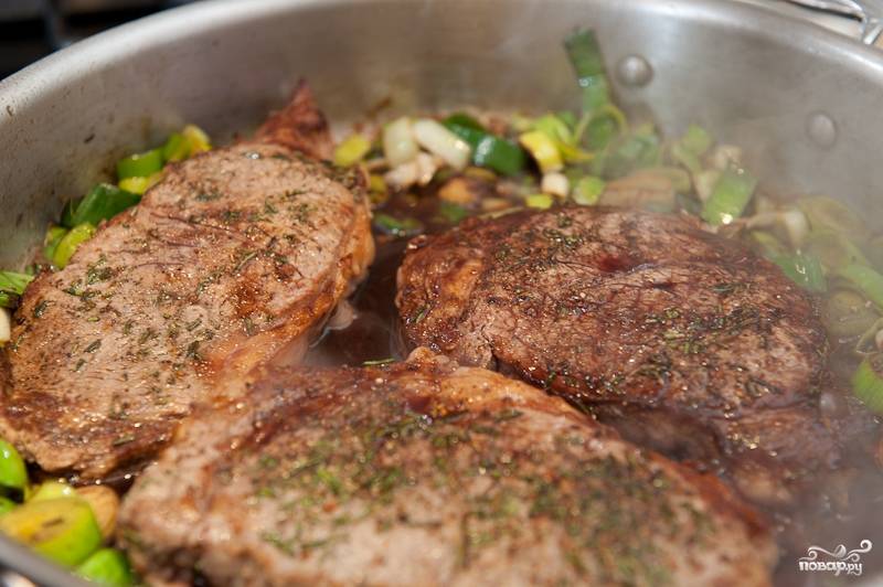 Прижмите лук-порей к краям сковороды, затем выложите стейки обратно. Полейте сцеженным соусом и буквально минуту подержите на плите, чтобы мясо успело прогреться.