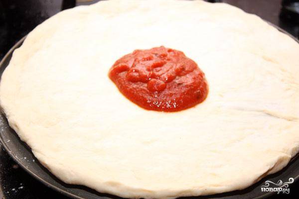 Теперь приступаем непосредственно к пицце. Раскатываем тесто до желаемого размера и толщины, равномерно смазываем его томатным соусом (или другим соусом для пиццы).