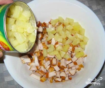 Выкладываем курицу в удобную салатницу. Открываем консервированные ананасы, сливаем жидкость, она нам не понадобится. Добавляем готовые квадратики из ананасов в куриную нарезку.