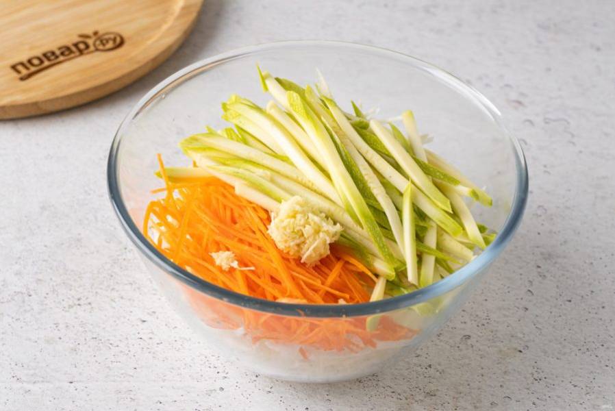 Морковь очистите и натрите на терке для моркови по-корейски. Кабачок нарежьте брусочками или тоже натрите на корейской тёрке. Чеснок мелко измельчите. Объедение все овощи в большой миске и аккуратно перемешайте.