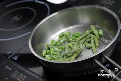 В сковородку наливаем немного растительного масла и обжариваем в нем спаржу и зеленый горошек.