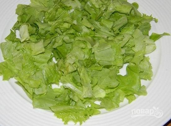 Салатные листья помоем и обсушим, а затем порвем руками на кусочки и выложим на тарелку.
