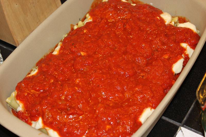 6. Выложить томатный соус и разровнять его так, чтобы он покрыл все каннеллони. Осталось только натереть на средней терке сыр и присыпать им блюдо сверху. 